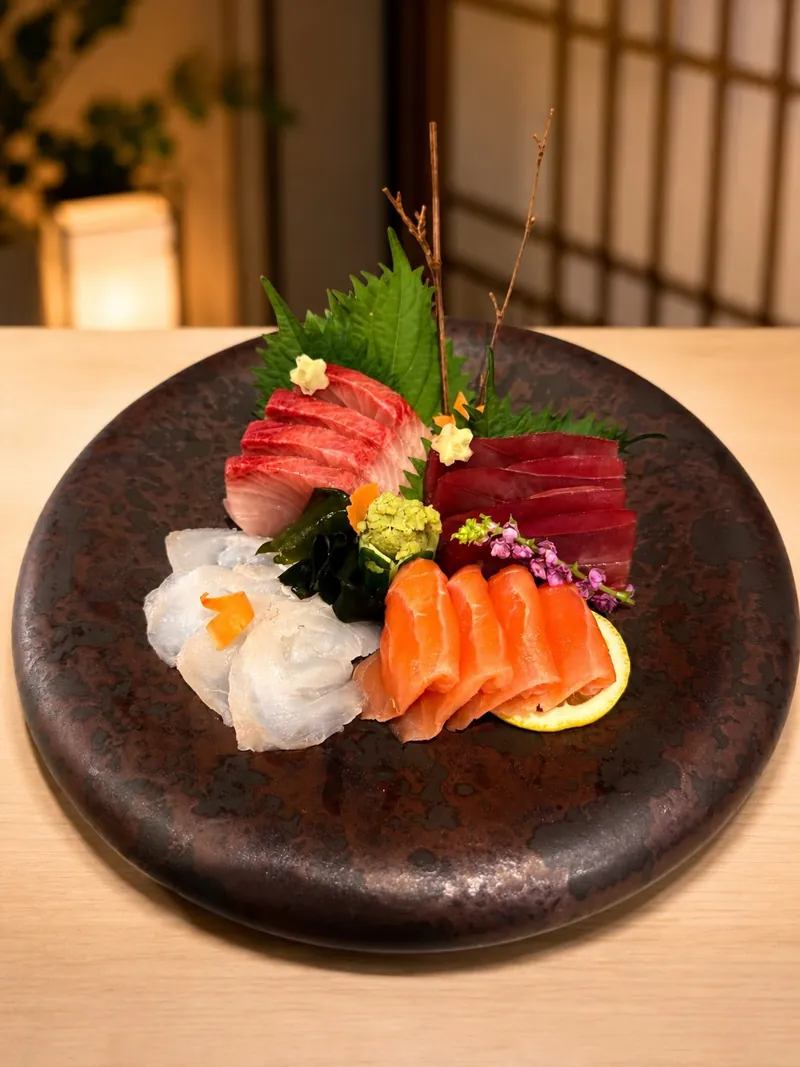 Sashimi de William Utida: cortes de pescado, folhas verdes e flores sobre cerâmica escura